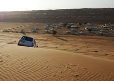 A car approaching a small town of tents in the middle of the desert.