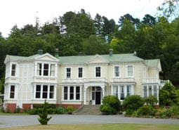 The Oruawharo Homestead as seen from the front yard with its white facade and towering trees from behind.