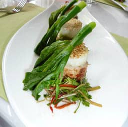 A plate with the delicious Garden's Chicken Rice with edible leaves placed on top and some herbs beside it.